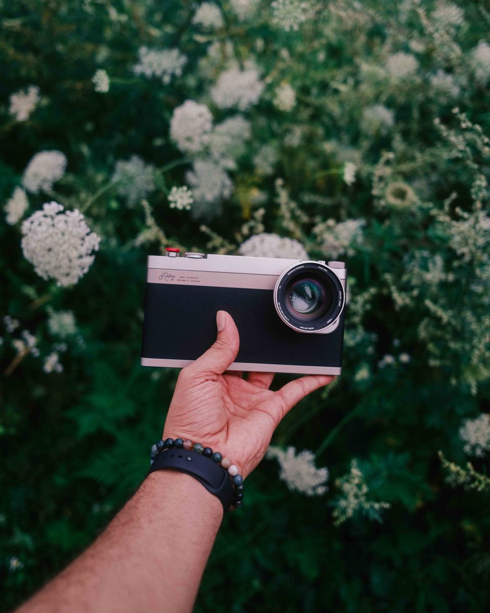 Fotorgear retro camera case with mobile lens mounted, held against wildflowers